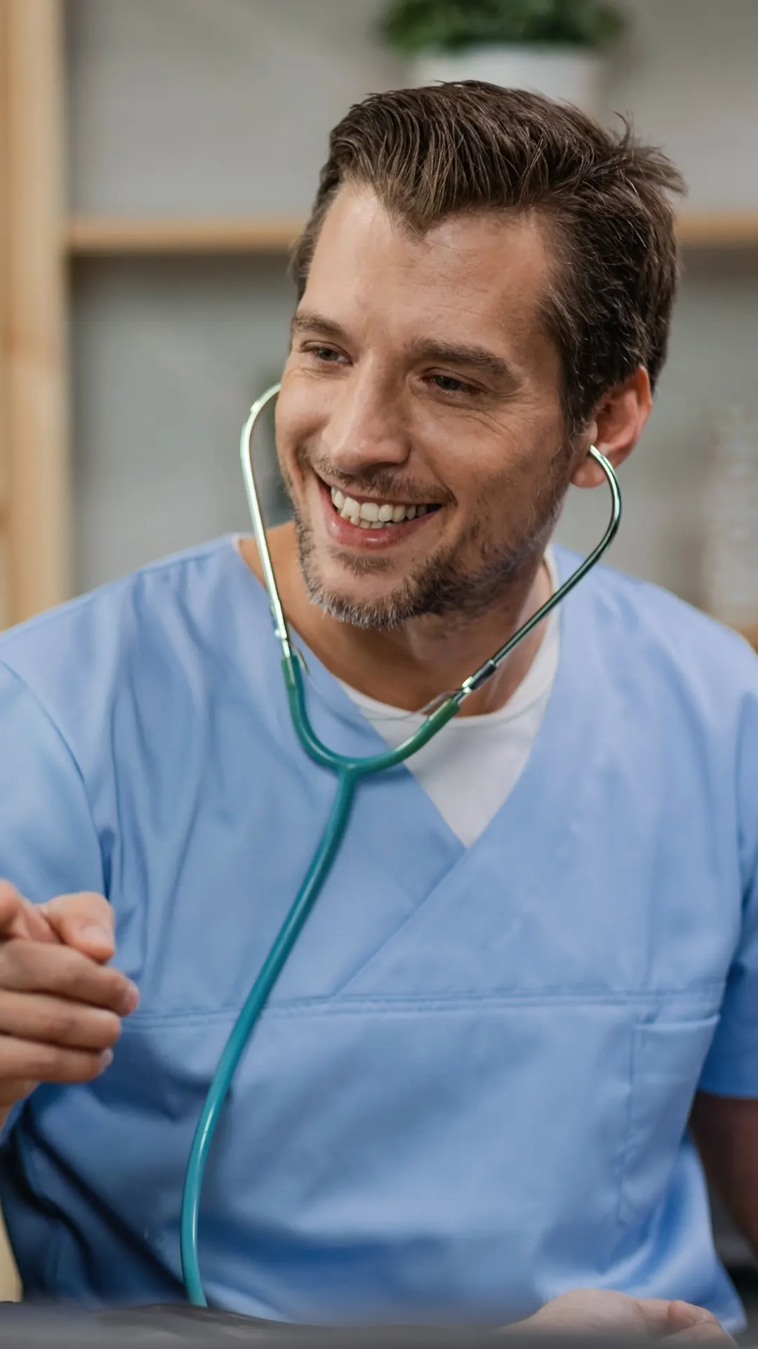 A smiling doctor in blue scrubs talking with an older patient during a home visit
